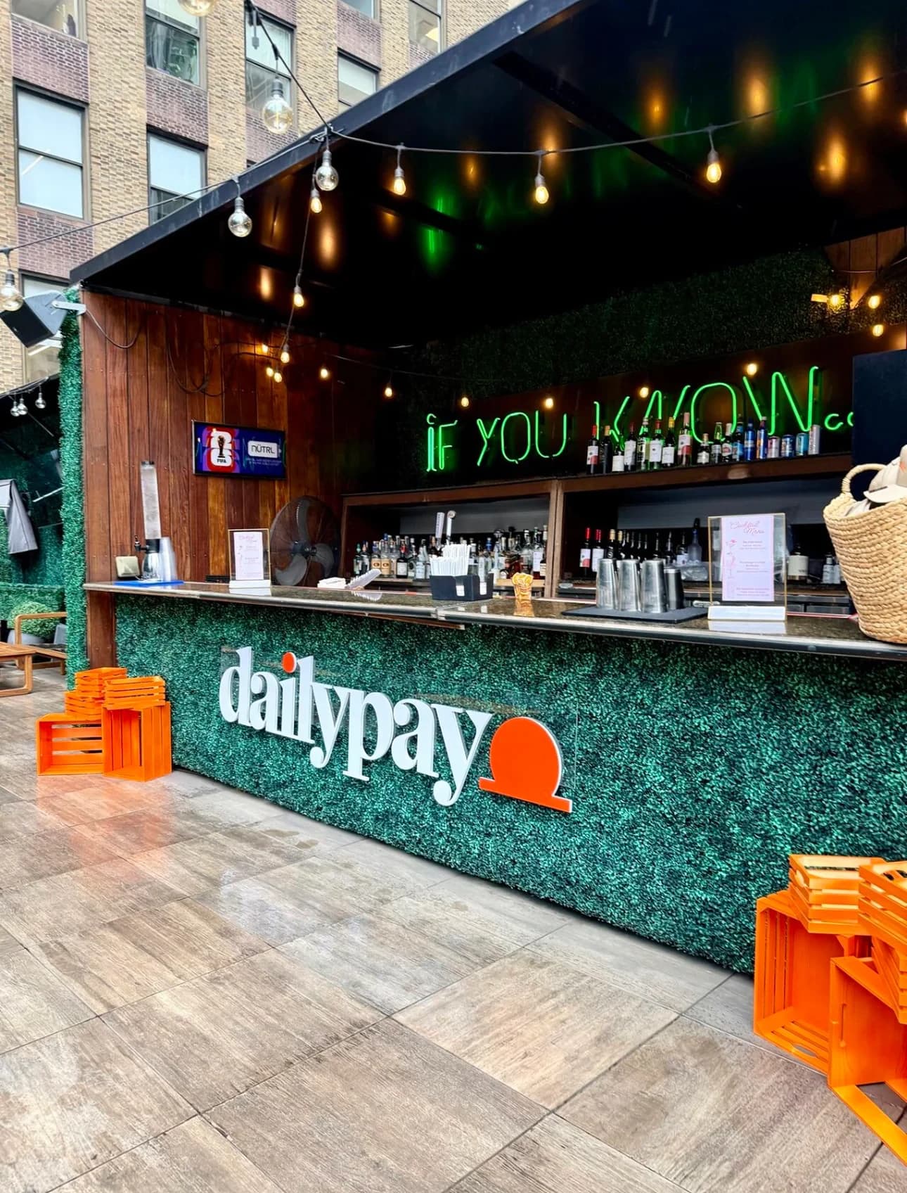 An outdoor bar with a DailyPay logo on the green hedge frontage at a brand activation