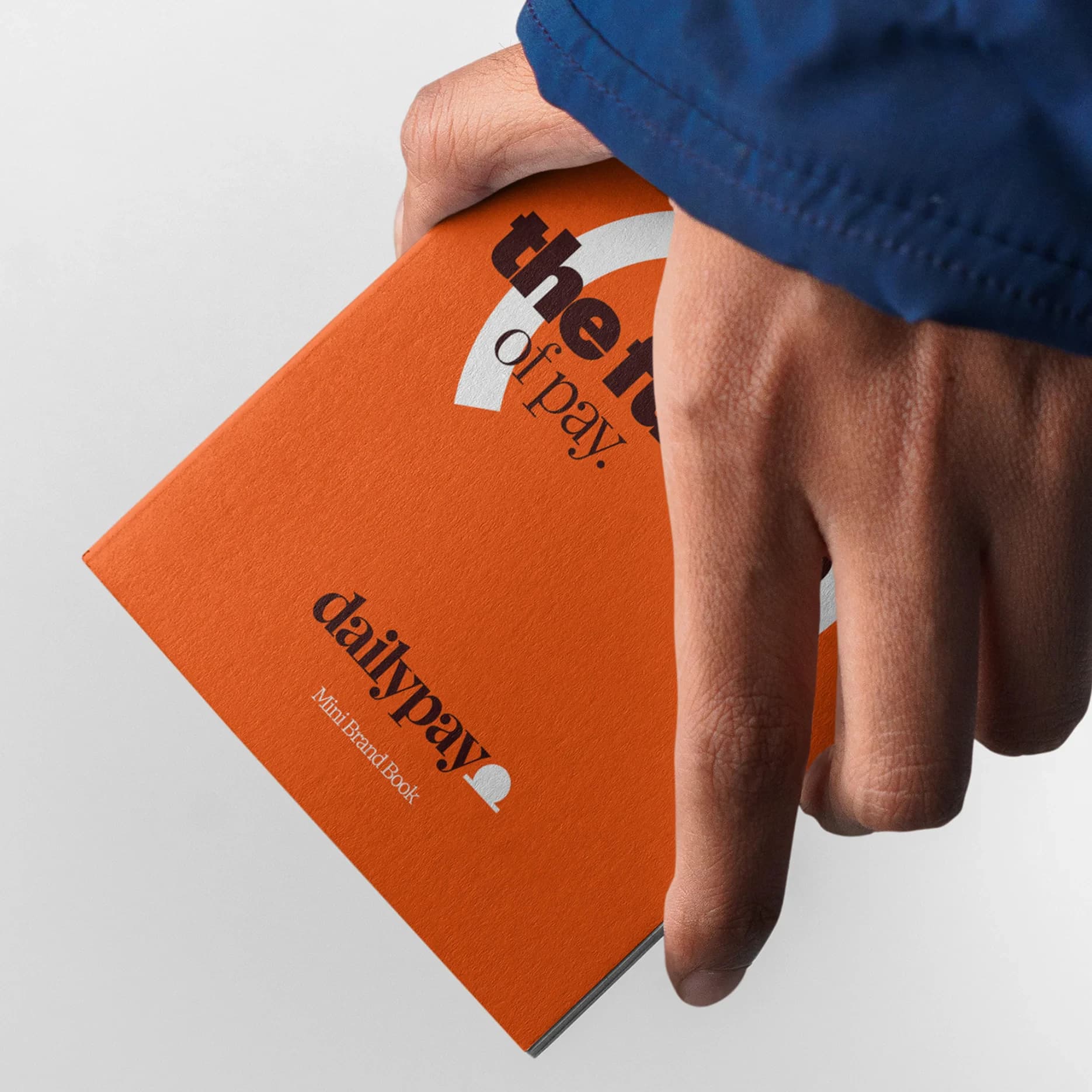 A hand holding the orange DailyPay Mini Brand Book