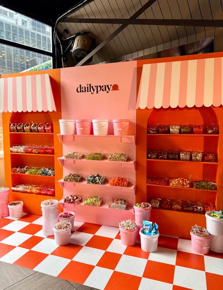 A pink and orange DailyPay-branded pick-and-mix sweet stall at a brand activation