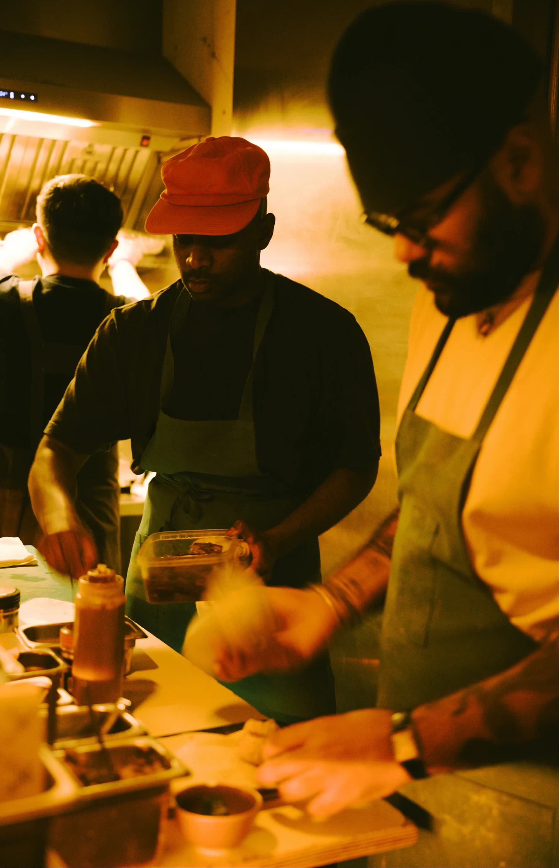 Two chefs plating food on a busy restaurant kitchen pass under warm light