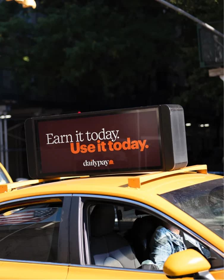 A yellow New York taxi with a rooftop LED screen reading 'Earn it today. Use it today.'